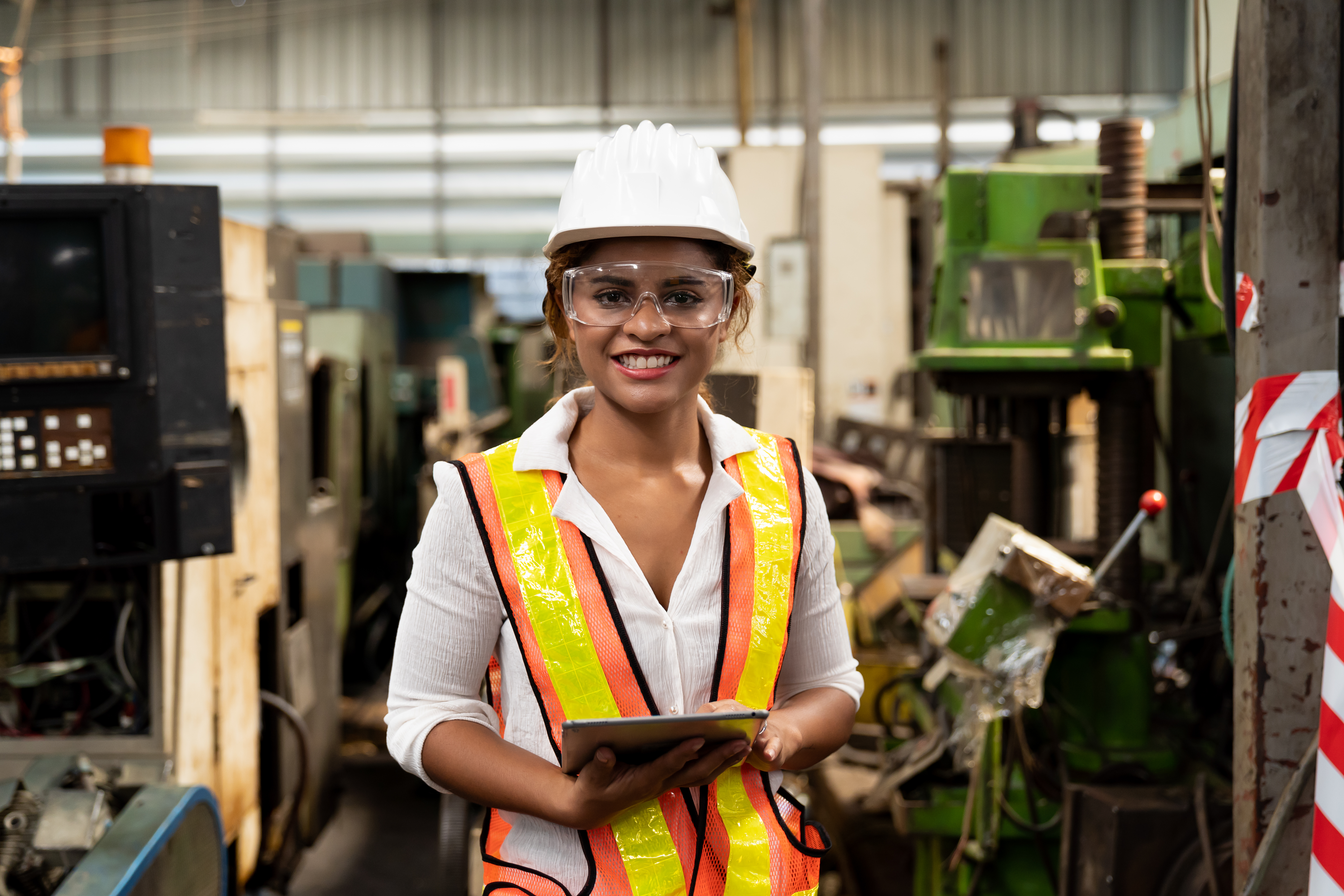 Woman stands by engineering equipment wearing a hard hat and goggles