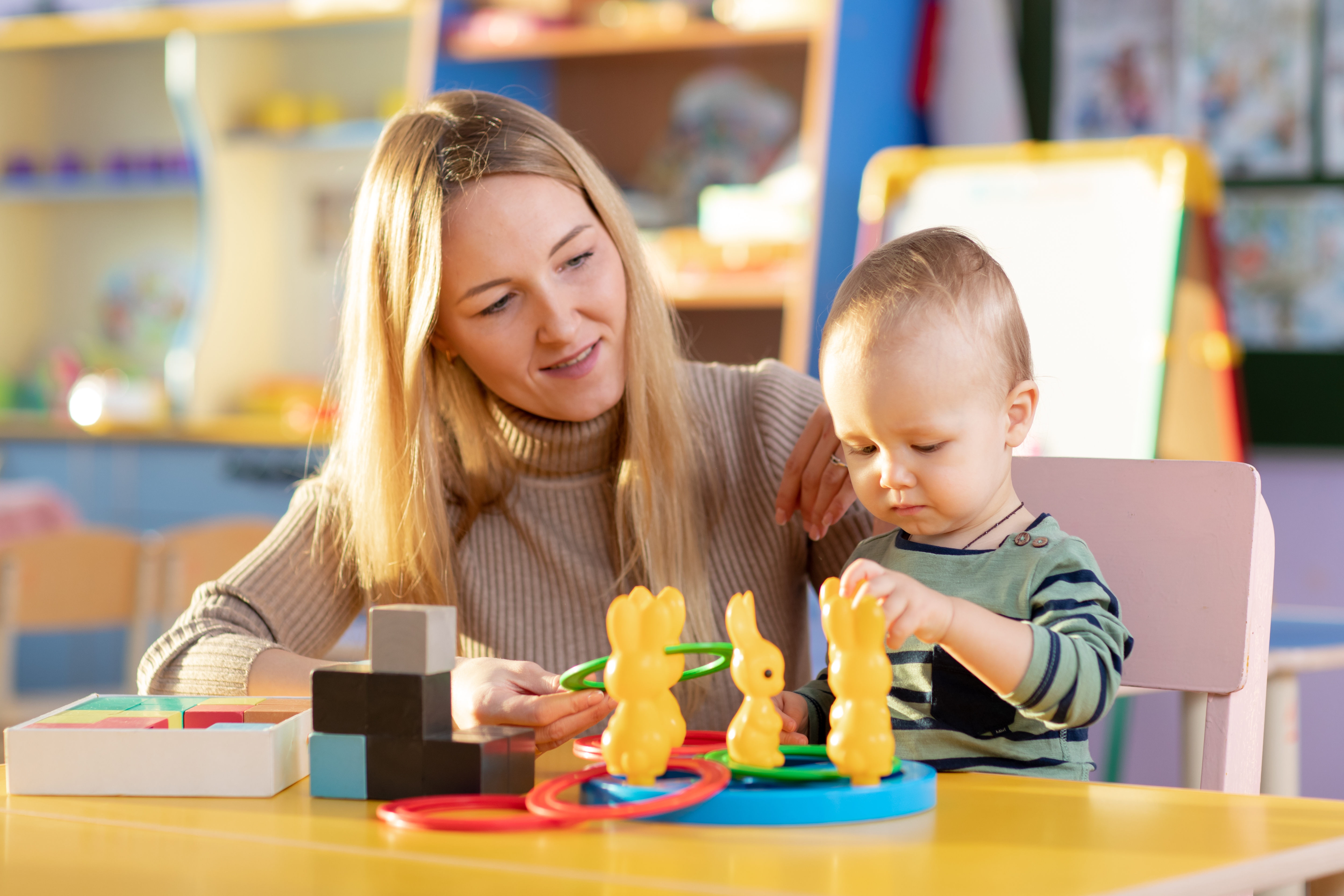 Early years teacher sits playing with younger learner